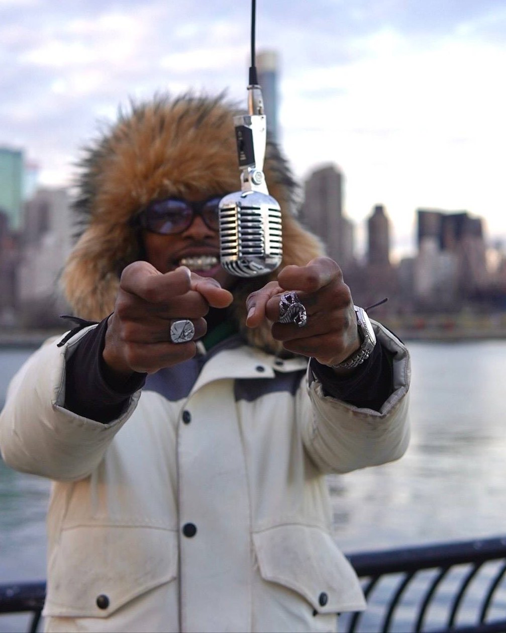 Pharaoh Linc pointing at the camera behind a vintage microphone, New York skyline behind him